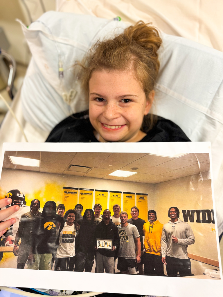 Gianna holds the photo of the Hawkeye Football team with the Believe sign